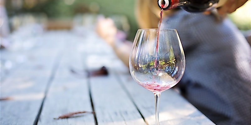 Person gießt Rotwein in Langstielglas ein