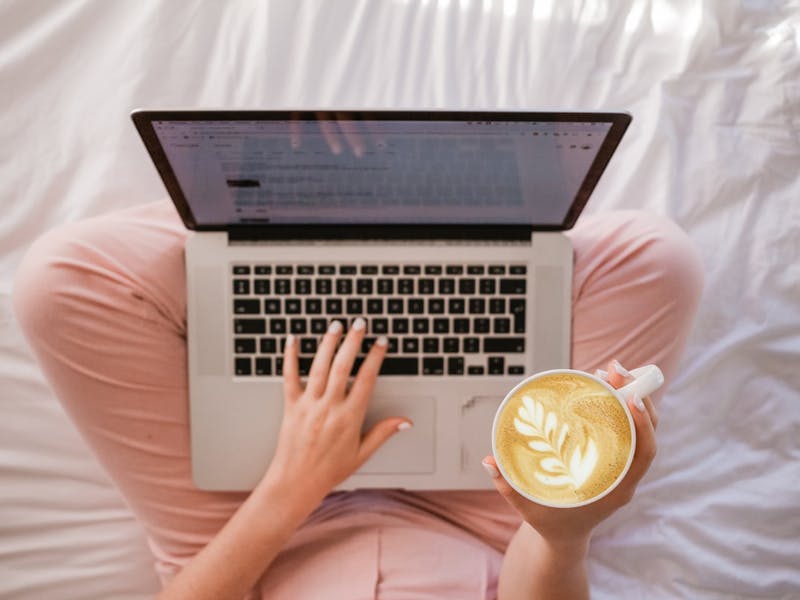 Eine Frau arbeitet am Laptop und hält eine Tasse Kaffee in der rechten Hand