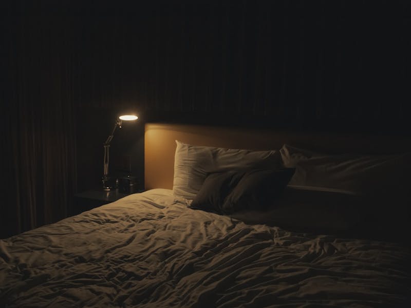 Ein Bett mit der weißen Bettwäsche und ein Nachttisch mit einer Lampe darauf