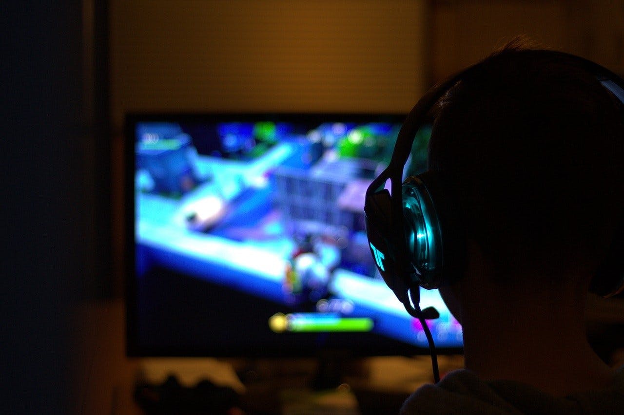 Jugendlicher mit Kopfhörer sitzt vor erleuchtetem PC Bildschirm und zockt
