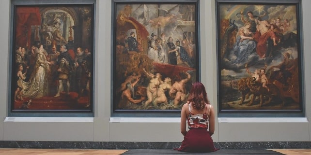 Frau sitzt in Museum und schaut sitzend drei Bilder an Frau sitzt in Museum und schaut sitzend drei Bilder an