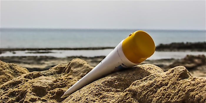 Reiseapotheke_Sonnencreme Tube Sonnencreme liegt im Sand am Meer