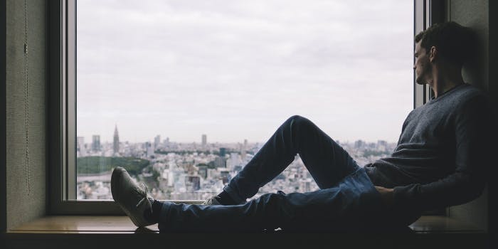 Mann sitzt allein auf einer Fensterbank und blickt auf eine Stadt herab
