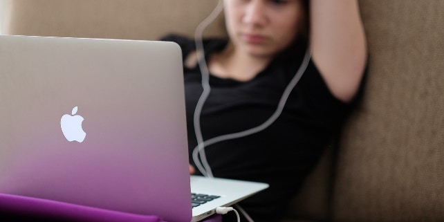 BCO_Norton_Mac Mädchen sitzt auf dem Sofa an ihrem Mac mit Kopfhörern