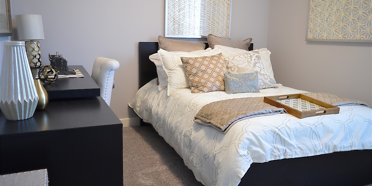 Schlafzimmer mit Bett und vielen Kissen sowie einem dunklen Sideboard