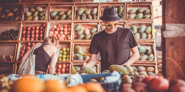 Mann mit Sonnenbrille und Hut wählt Obst im Supermarkt aus