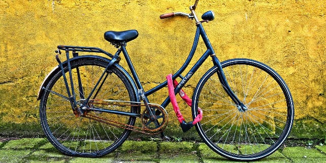 Schwarzes Cityrad mit pinkem Fahrradschloss an gelbe Wand gelehnt
