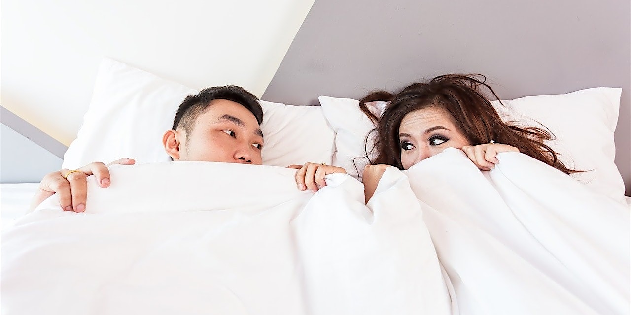 Passion Dreams Gutschein Pärchen liegt zusammen unter der Bettdecke und schaut sich tief in die Augen