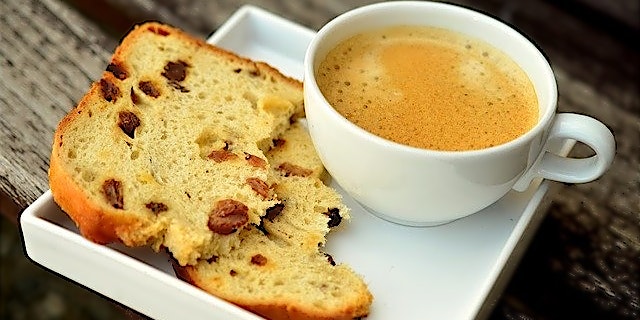 Scheibe Rosinenbrot an Kaffee in weißem Kaffeeservice mit quatratischer Untertasse.