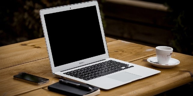 Neben einem weißen Laptop stehen ein Espresso, ein Smartphone und ein Notizblock Neben einem weißen Laptop stehen ein Espresso, ein Smartphone und ein Notizblock