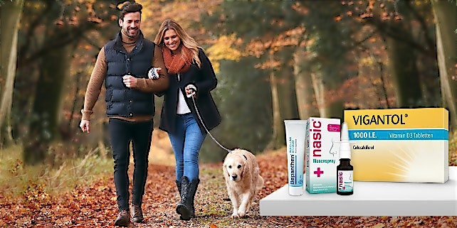 Ein Pärchen geht mit seinem Hund im Wald spazieren.