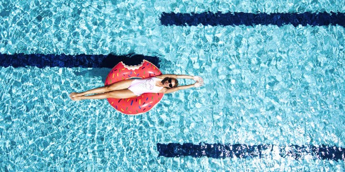Frau liegt im Badeanzug auf einem Donut-Schwimmring im Pool