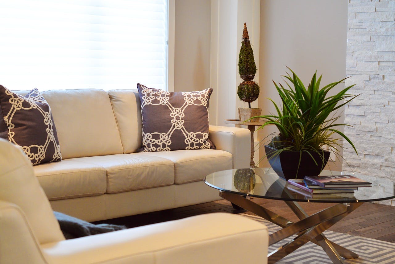 Beige Couchecke in hellem Wohnzimmer mit rundem Glastisch und Zimmerpflanzen