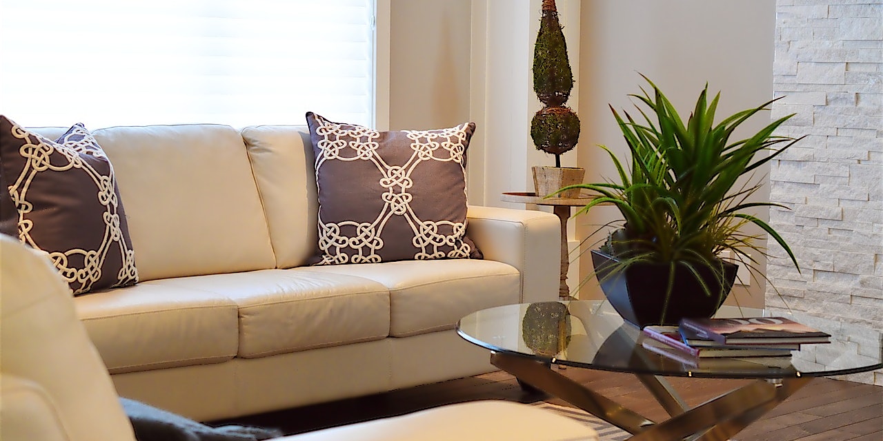 Beige Couchecke in hellem Wohnzimmer mit rundem Glastisch und Zimmerpflanzen