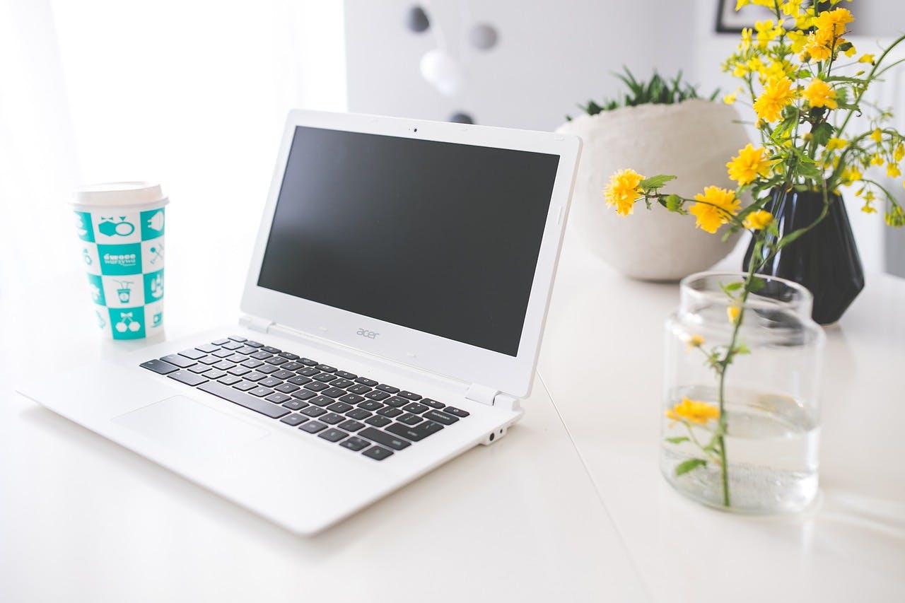 Acer Gutschein Aufgeklappter Acer Laptop auf einem Tisch stehend neben einer Blume und einem Kaffee to go Becher