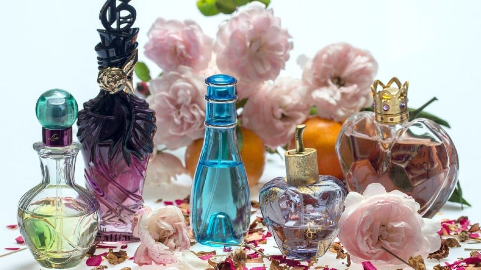 Fünf verschiedene Parfums umgeben von Rosen und Orangen