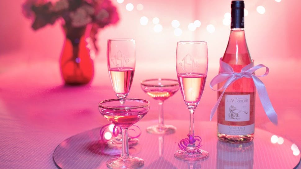 Champagnerflasche mit Gläsern vor rosa Hintergrund
