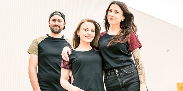 Zwei Frauen umarmen sich, ein Mann steht lässig daneben