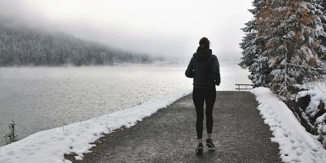 Frau joggt am See, es liegt Schnee