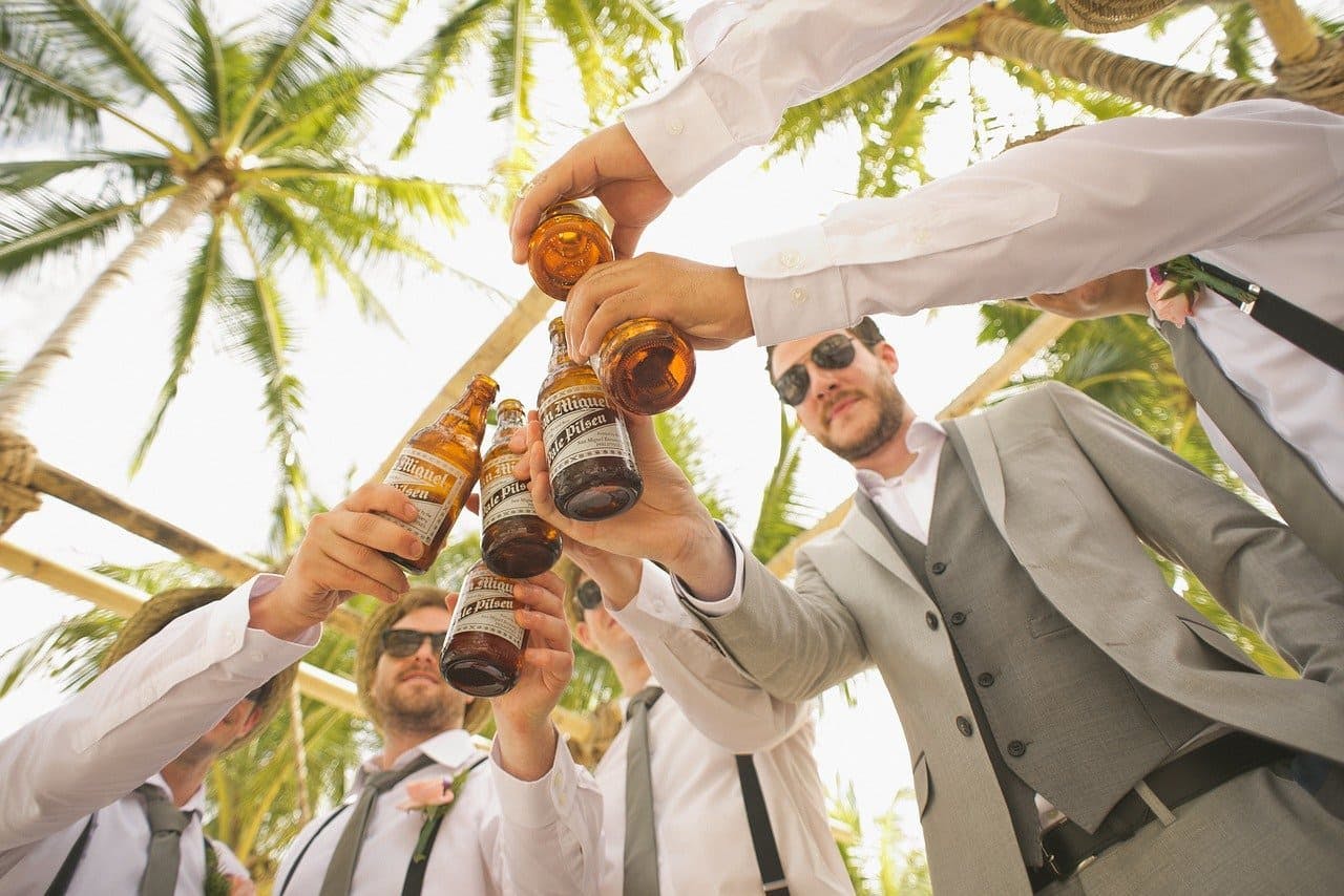 Männer im Anzug stoßen mit Bier unter Palmen an